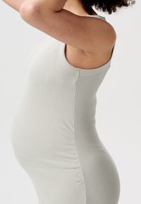 Těhotenské šaty z lehké šedé žebrované látky. Přiléhavý střih bez rukávů s bočním nařasením, zvýrazňující zaoblenou siluetu.