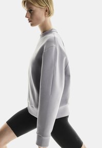 Sweatshirt gris avec un col rond et des poignets côtelés, assorti à des short de vélo noirs. Texture lisse avec un minimum de branding sur la poitrine.