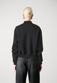 Sweat-shirt noir avec un col montant, des épaules tombantes et un ourlet côtelé. Associé à un jean en denim foncé taille haute. Texture subtile.