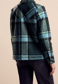 Zielono-niebieska koszula flanelowa w kratę z kołnierzykiem, teksturowany materiał oraz detal w tyle, w połączeniu z ciemnymi dżinsami.