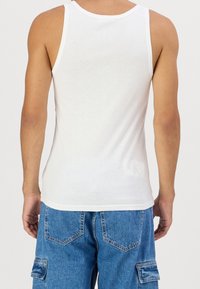 Top sin mangas de algodón blanco con escote redondo y tirantes anchos, combinado con pantalones cortos cargo de mezclilla azul con bolsillos de parche.