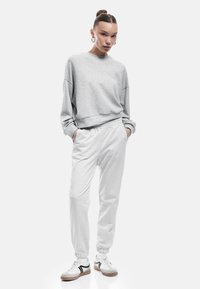 Lichtgrijze sweatshirt met verlaagde schouders, gecombineerd met lichtgrijze tapered sweatpants met een elastische tailleband, gedragen met witte sneakers.