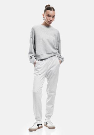 Lichtgrijze sweatshirt met verlaagde schouders, gecombineerd met lichtgrijze tapered sweatpants met een elastische tailleband, gedragen met witte sneakers.