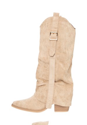 Stivaletti beige in suede con design morbido, punta appuntita, tacco largo e cinturino con fibbia metallica sul lato esterno.