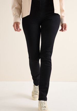 Mustat slim fit -farkut, joissa on sileä pinta, keskipitkä vyötärö ja kapeat lahkeet. Yhdistetty vaaleisiin urheilujalkineisiin.