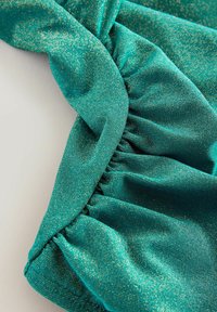 Teal stof met een glinsterende, metalen textuur en geplooide details. Het materiaal is glad met fijne gouden stippen verspreid over het oppervlak.
