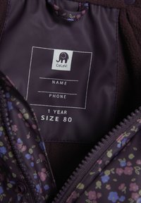 Fialová podšívka s květinovým vzorem, obsahující vnitřní štítek s grafickým logem, velikost 80 a místy pro jméno a telefon.