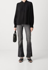 Blusa nera plissettata con scollatura a ruches, abbinata a jeans grigi a palazzo, sandali neri con tacco e una piccola borsa nera.