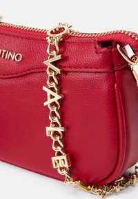 Červená kožená crossbody taška so zlatým reťazovým popruhom s písmenkovými akcentmi. Zips s textúrovaným povrchom a detailom loga.