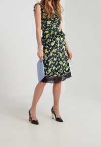 Blommig klänning med svart spetsnederdel, prydd med gula citroner och gröna detaljer. Matchad med svarta klackskor och en blå kuvertväska.