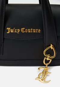 Sac en cuir noir avec le logo "Juicy Couture" en or, des accessoires en forme de cœur et un charme en or avec un design de lettres entrelacées.