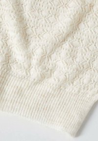 Tissu tricoté couleur crème avec un motif texturé en diamant et un bord côtelé, probablement une manche ou un détail d'ourlet de pull.