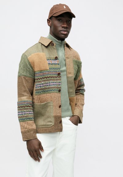 Casaco patchwork multicolorido com tecidos texturizados em verde, bege e castanho, com frente de botões e grandes bolsos. Usado sobre uma blusa verde.