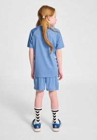 Ljusblå idrottsdräkt bestående av en kortärmad tröja och shorts, i kombination med vita strumpor med svarta chevronmönster och blå skor.