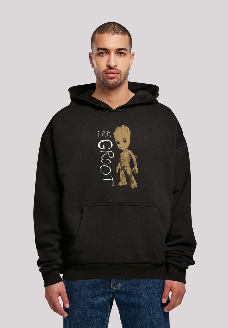 Svart hettegenser med teksten "I AM GROOT" og grafikk av en karakter med en brun, trelignende tekstur og grønne aksenter. Design med kengurulomme.