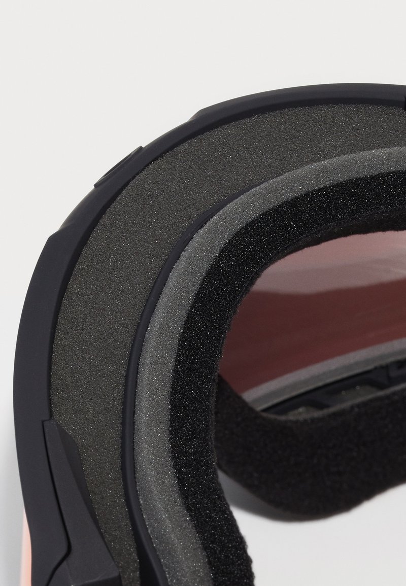 Détail du casque avec un rembourrage en mousse stratifié, des accessoires en métal noir et un intérieur lisse et réfléchissant dans des nuances de gris et de rose.