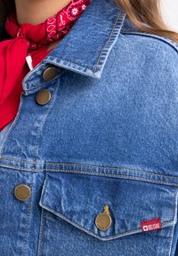 Sinine denim jakk kullast riistvara, nähtavate õmblustega ja punase "BIG STAR" sildiga taskul. Omab klassikalist krae ja esipnuppe.