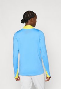 Πουκάμισο μακρυμάνικο σε ανοιχτό μπλε χρώμα με κίτρινο γιακά και μανσέτες. Κατασκευασμένο από λείο ύφασμα με εφαρμοστή γραμμή και χωρίς ορατά σχέδια.