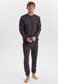Mørkegrå pullover med V-hals og rundt logo, kombineret med matchende joggers med elastiske manchetter; glat tekstur og afslappet pasform.