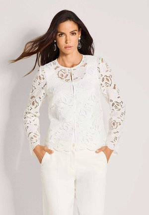 Witte kanten jas met lange mouwen, een geschulpte zoom en decoratieve bloemmotieven. De stof is doorschijnend met een knoopsluiting aan de voorkant.