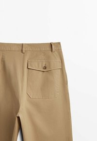 Chinos en coton beige avec une coupe droite, poche arrière avec fermeture à bouton et passants de ceinture pour un ajustement réglable. Texture lisse.