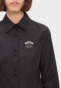 Camicia nera con bottoni a punta, caratterizzata da un logo ricamato Moschino Jeans e tessuto testurizzato con una finitura liscia.