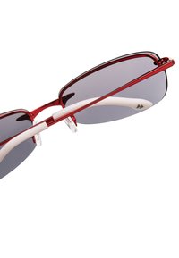 Occhiali da sole con una montatura in metallo rosso, lenti grigie e dettagli bianchi sulle astine. Presentano un design curvo e naselli trasparenti per il massimo comfort.