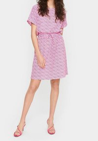 Rosa kortärmad klänning med svart hjärt-mönster, knytning vid midjan och lös passform. Kombinerad med rosa sandaler med remmar.