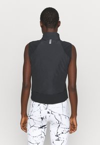 Chaleco negro sin mangas con cuello alto, tela ligera, diseño ajustado y dobladillo elástico; cuenta con detalles reflectantes en la parte posterior.