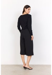 Black long-sleeve top with a wide neckline paired with black culotte pants. The outfit features a relaxed fit and smooth texture. Black strappy heels complete the look.