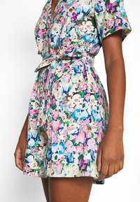 Kwiatowa sukienka o krótkim fasonie, wykonana z lekkiego materiału w odcieniach różu, niebieskiego i zielonego, z przewiązanym w pasie i kołnierzykiem.