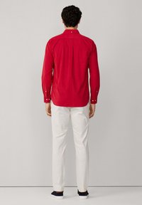 Rode blouse met lange mouwen en een button-down kraag, rugplooien en witte knopen, gecombineerd met witte broek en donkere sneakers.