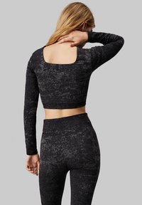 Top nero a maniche lunghe e taglio corto con scollatura quadrata sul retro, abbinato a leggings a vita alta coordinati, caratterizzati da un motivo testurizzato.