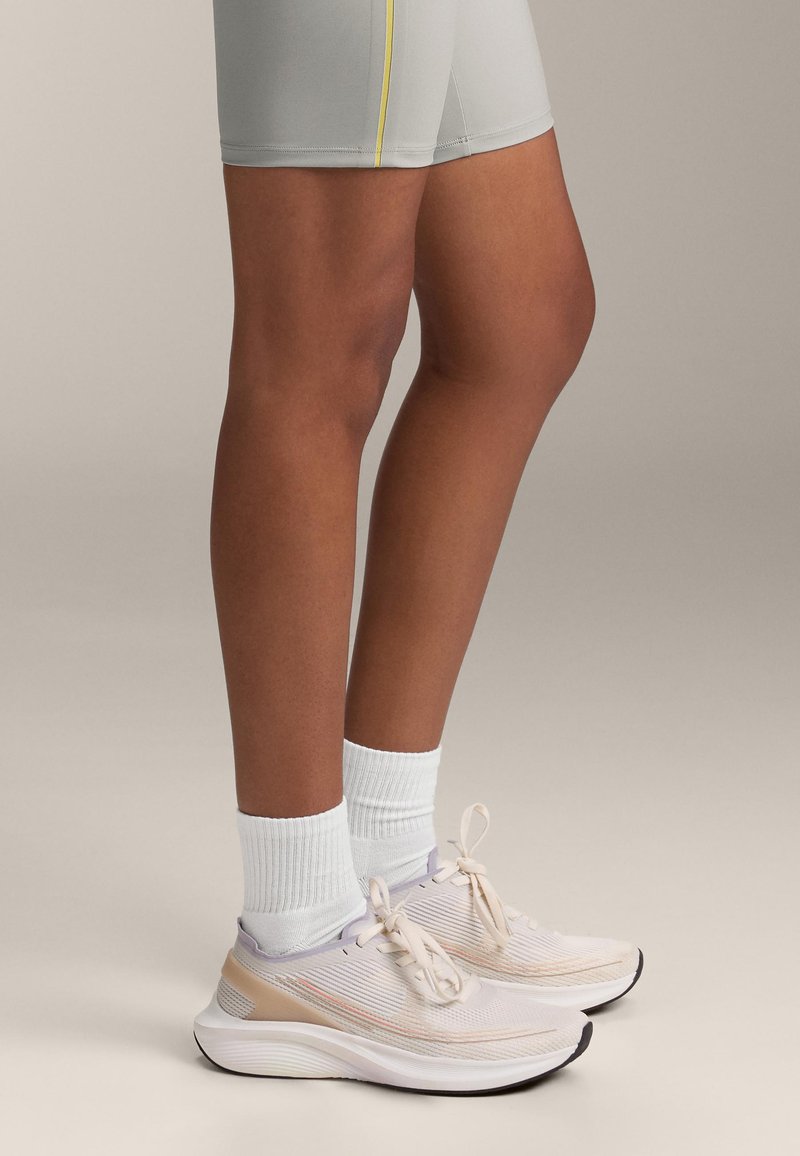 Světle šedé sportovní šortky se žlutým švem, doplněné bílými žebrovanými ponožkami a světlými béžovými běžeckými botami s texturovaným designem a šněrováním.