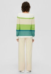 Sweter z długim rękawem, w kolorowe bloki z poziomymi paskami w białym, zielonym i niebieskim kolorze, połączony z kremowymi spodniami o szerokich nogawkach i białymi trampkami.