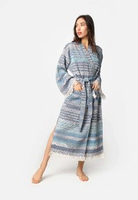 Dolga obleka z modrim in sivo vzorcem ter resicami ob robovih, izdelana iz teksturirane tkanine, vsebuje zavezan pas in zvonaste rokave.