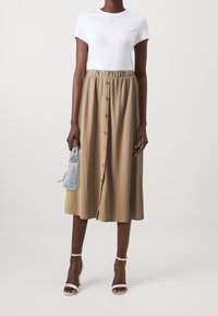 Gonna midi khaki con bottoni frontali, cintura elastica, abbinata a una t-shirt bianca e una piccola borsa a tracolla azzurro chiaro. Indossata con sandali bianchi con tacco.