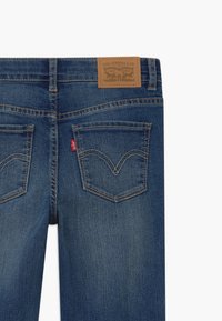 Jeans de denim azul oscuro con dos bolsillos traseros, costuras visibles y un parche de cuero marrón de la marca en la cinturilla.