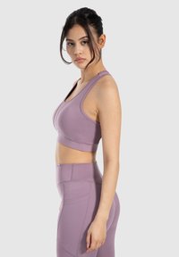 Sostén deportivo morado hecho de tela elástica, con tirantes anchos y una banda de soporte. Combinado con leggins de cintura alta a juego que cuentan con bolsillos laterales.