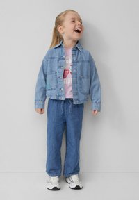 Veste en denim avec fermeture à boutons, deux poches avant et coutures bleues. Associée à un t-shirt graphique rose clair et à un jean large bleu.
