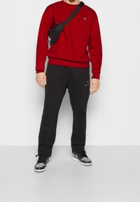 Sudadera roja con puños y dobladillo acanalados, pantalones jogger negros con un diseño elegante, y zapatillas con estampado en tonos gris y negro. Bolsa cruzada negra.