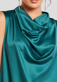 Top de satén verde azulado con un escote drapeado y textura suave. Presenta un cierre oculto y diseño sin mangas, resaltando el brillo de la tela.