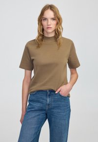 Bruine t-shirt met korte mouwen en een hoge halslijn, gecombineerd met lichtblauwe denim jeans. De stof lijkt glad en aansluitend.