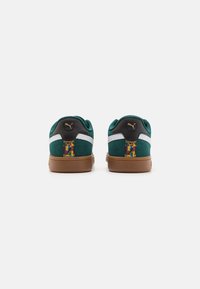 Sneakers in suede verde con accenti neri, strisce laterali bianche e dettagli colorati sul tallone. Suola piatta in gomma marrone. Punta arrotondata.