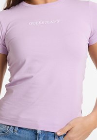 Licht paarse, getailleerde t-shirt van zachte katoen, met korte mouwen en een witte "GUESS JEANS" logo, centraal op de borst.