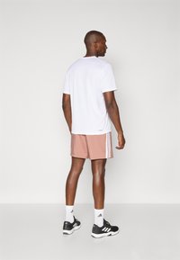 Hvid atletisk T-shirt, pink shorts med hvide sidelange striber, sorte sneakers og hvide sokker, set fra ryggen mod en neutral baggrund.