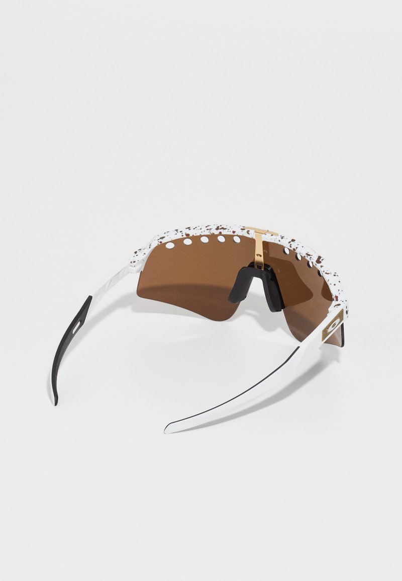 Zonnebril met een bruine lens, wit frame met een gestructureerde strook, zwarte accenten en een gouden scharniertje.