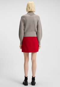 Person with short blonde hair wearing a gray ribbed sweater, red skirt, black socks, and black platform shoes, viewed from behind.