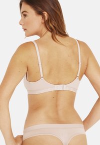 Soutien-gorge rose clair avec bretelles ajustables et fermeture à crochets. Tissu lisse et design minimaliste, associé à une culotte assortie rose clair.