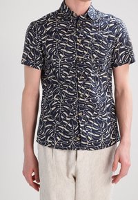 Camicia a maniche corte di colore blu navy con un motivo fogliare bianco. Presenta un colletto con bottoni e cinque bottoni frontali, realizzata in un tessuto leggero.